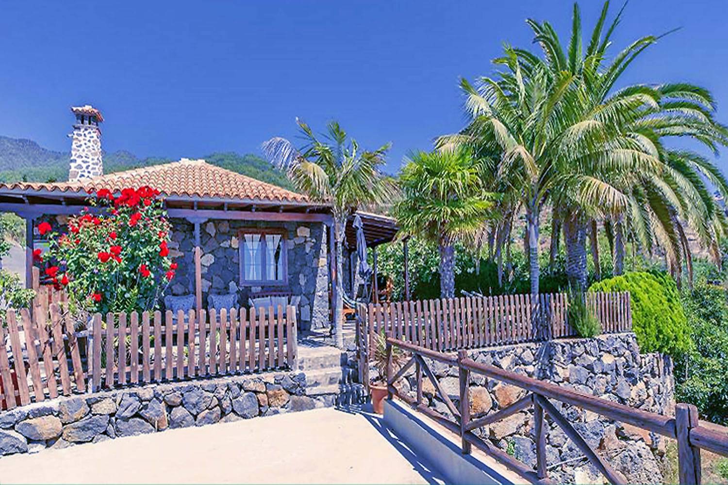 Rustikales und komplett renoviertes Haus mit einer Inneneinrichtung, die Holzelemente und warme Farben kombiniert, und einem schönen Garten mit erfrischenden Palmen